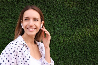 Kablosuz kulaklıklı genç bir kadın yeşil çim duvarın yanında müzik dinliyor. Metin için boşluk