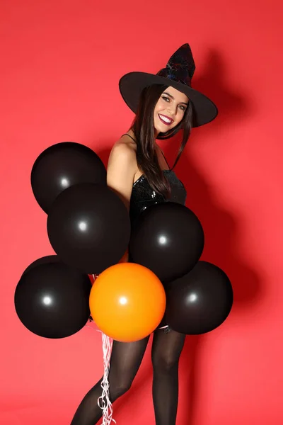 Frumoasă femeie tânără purtând costum de vrăjitoare cu baloane pentru petrecerea de Halloween pe fundal roșu — Fotografie, imagine de stoc