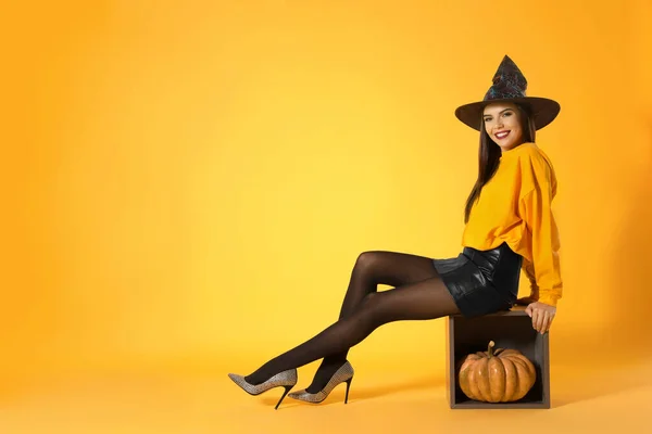 Mulher bonita vestindo traje de bruxa para festa de Halloween com abóbora contra fundo amarelo, espaço para texto — Fotografia de Stock