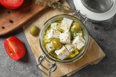 Düz kompozisyon, gri masanın üzerinde kavanozda beyaz peynir turşusu.