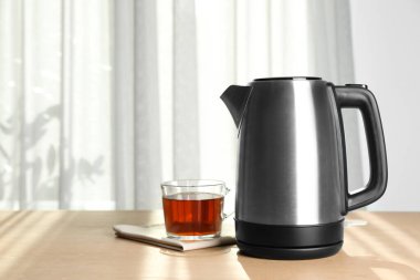 Modern elektrikli çaydanlık ve bir fincan çay içerideki ahşap masada. Metin için boşluk