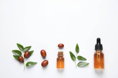 Glass bottles with jojoba oil and seeds on white background, top view clipart