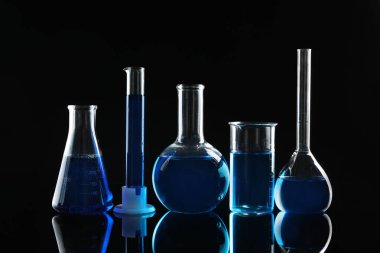 Siyah zemin üzerinde mavi sıvılar bulunan laboratuvar camları.