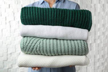Woman holding stack of warm clothes on white background, closeup. Autumn season clipart