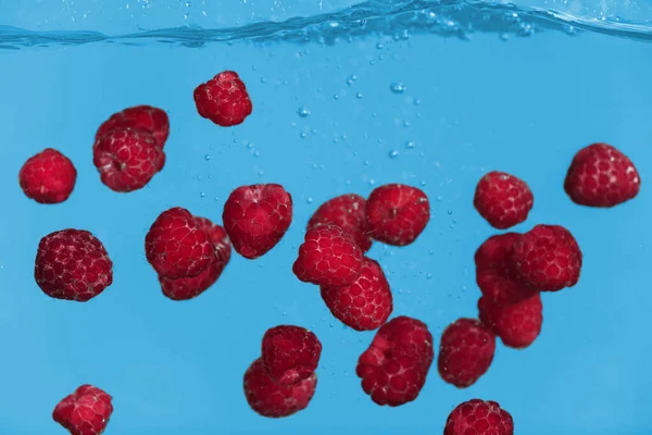 Frambuesas frescas maduras cayendo en agua sobre fondo gris —  Fotos de Stock