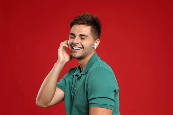 Happy young man listening to music through wireless earphones on red background — Stock Photo, Image