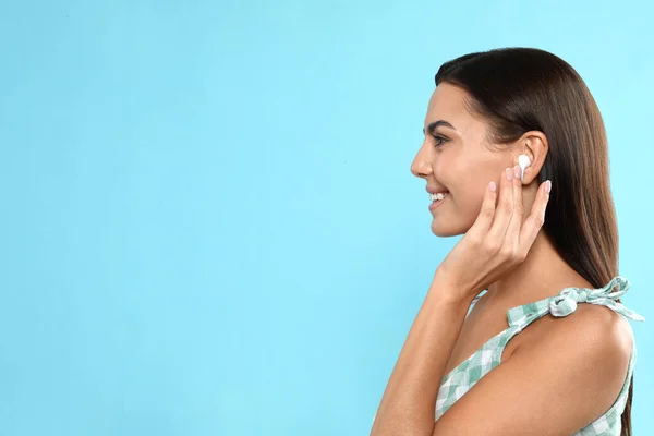 Mujer joven y feliz escuchando música a través de auriculares inalámbricos sobre fondo azul claro. Espacio para texto — Foto de Stock