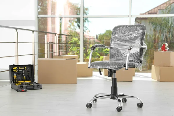 Chaise enveloppée dans le film et les effets personnels emballés dans le bureau, espace pour le texte. Service de déménagement — Photo