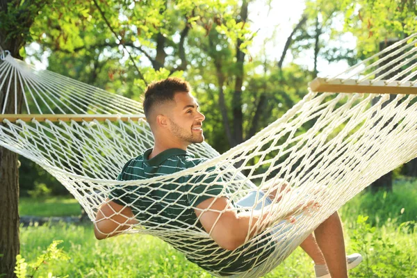 Молодой человек отдыхает в удобном гамаке в зеленом саду — стоковое фото