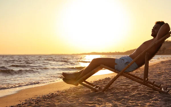 Giovane uomo rilassante sulla sedia a sdraio sulla spiaggia vicino al mare — Foto Stock