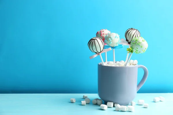Tasty cake pops in cup with marshmallow on wooden table against light blue background. Space for text — Stock Photo, Image