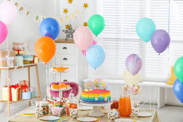 Bolo de aniversário brilhante e outras guloseimas na mesa no quarto decorado — Fotografia de Stock