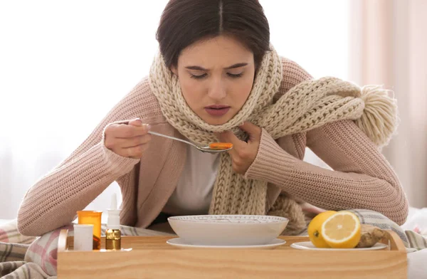 Больная молодая женщина ест суп, чтобы вылечить грипп дома — стоковое фото