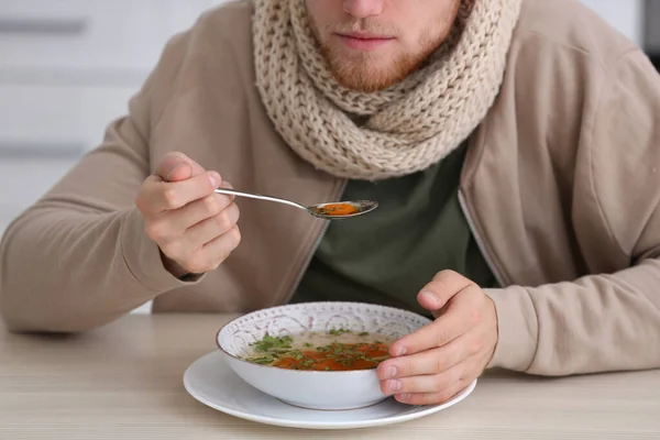 Sick young man eating soup to cure flu at table indoors — Stock Photo, Image