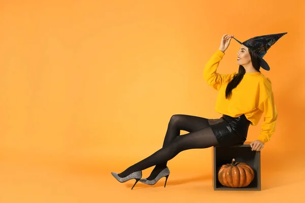 Hermosa mujer con traje de bruja para la fiesta de Halloween con calabaza sobre fondo amarillo, espacio para el texto —  Fotos de Stock