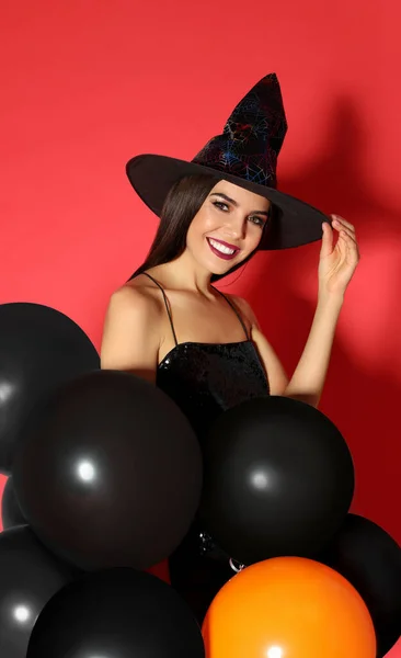 Gyönyörű fiatal nő visel boszorkány jelmez léggömbök Halloween party piros háttér — Stock Fotó