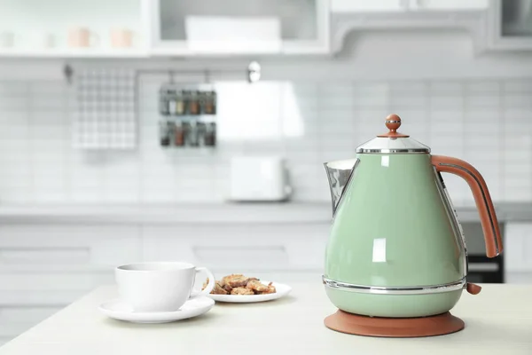 Modern electric kettle, cup and cookies on wooden table in kitchen — Stock Photo, Image