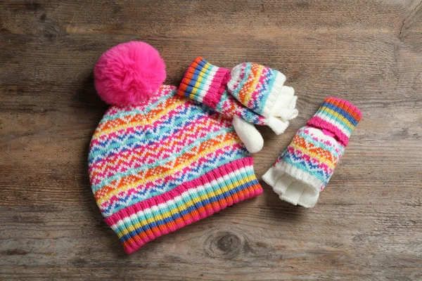 Warm knitted hat and mittens on wooden background, flat lay — Stock Photo, Image