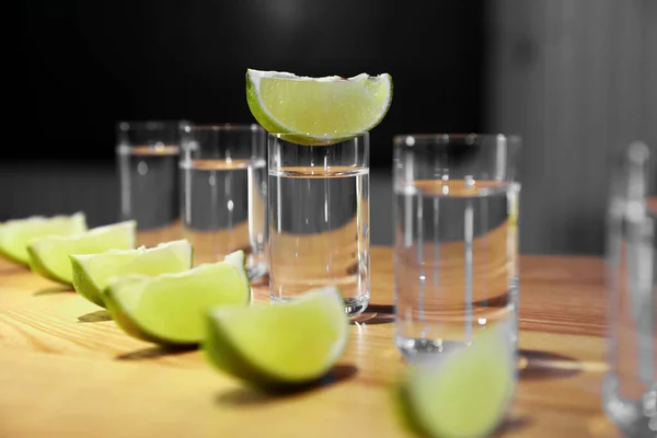 Vodka shots and lime slices on wooden bar counter, closeup — Stock Photo, Image