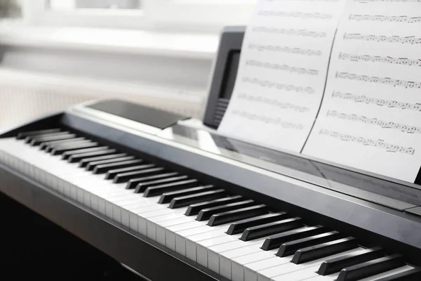 Modern piano with music sheets in room, closeup