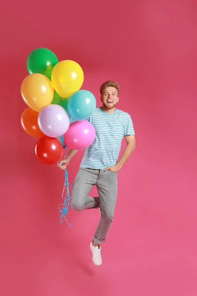 Young man jumping with bunch of colorful balloons on pink background — Stock Photo, Image