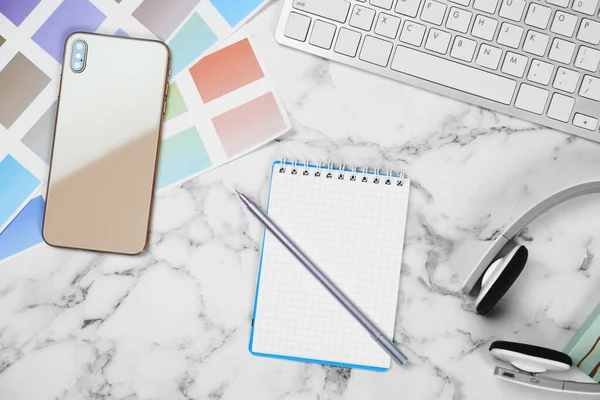 Composição de leigos planos com caderno, telefone e paletas de cores na mesa de mármore branco. Local de trabalho do designer — Fotografia de Stock