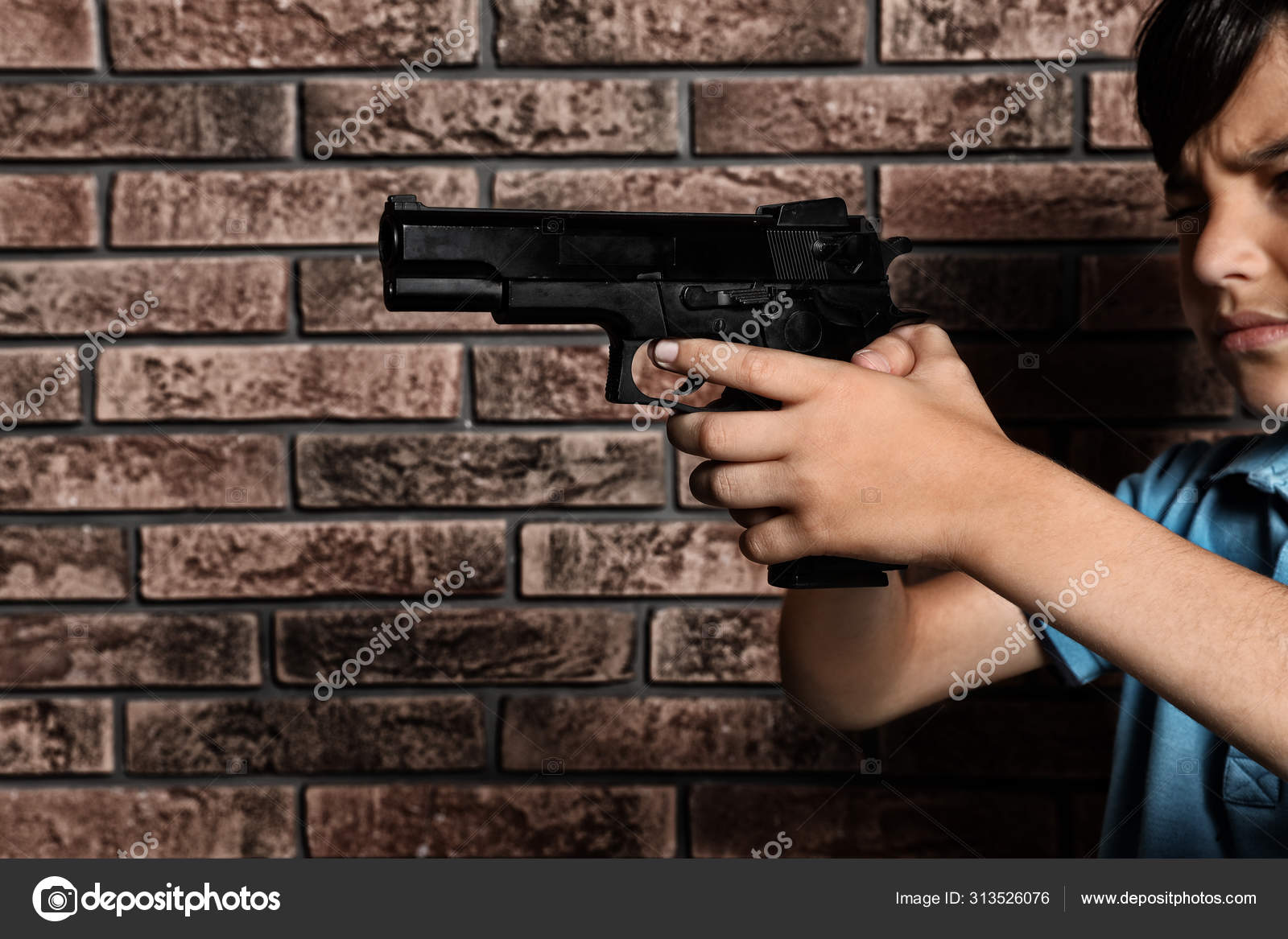 Little child playing with gun against brick wall