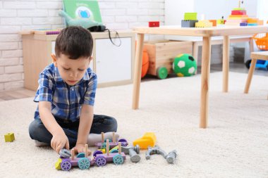 Adorable little boy playing with toys on carpet at home