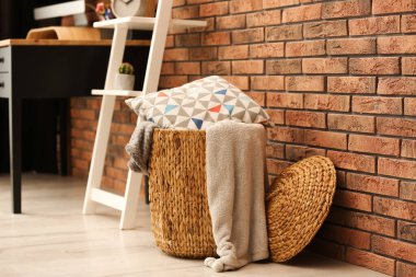 Wicker basket with blankets and pillow near brick wall, space for text. Idea for interior design