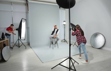 Asistan modern stüdyoda genç adamın fotoğrafını çeken profesyonel fotoğrafçı
