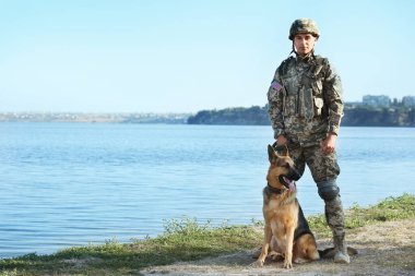 Nehir yakınında Alman çoban köpeği ile askeri üniformalı Adam, metin için alan