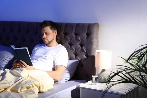 Красивый мужчина читает книги в темной комнате по ночам. Время спать — стоковое фото