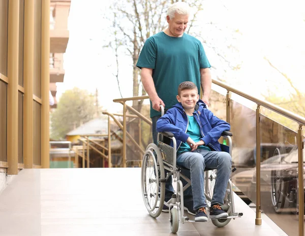 Niño preadolescente en silla de ruedas con su abuelo usando rampa al aire libre — Foto de Stock