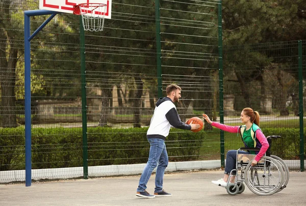 Mulher em cadeira de rodas e homem jovem jogando basquete em campo de esportes — Fotografia de Stock