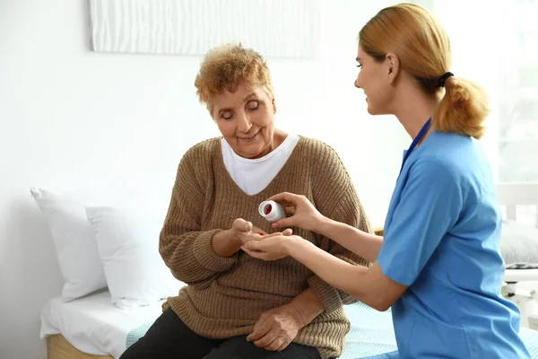 Krankenschwester verteilt Tabletten an ältere Frauen in geschlossenen Räumen. Medizinische Hilfe — Stockfoto