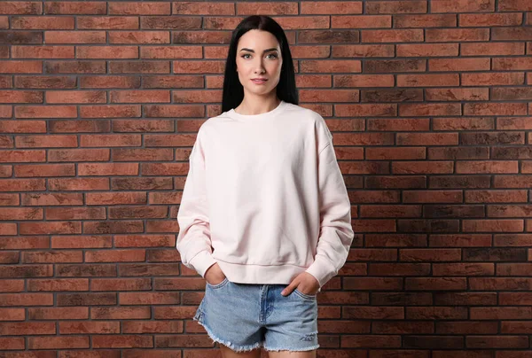 Porträtt av ung kvinna i tröja på tegelvägg. Mock-up för design — Stockfoto