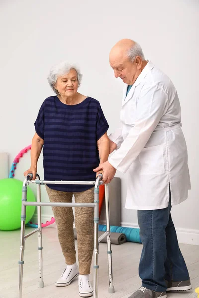 Orvos segít idős nő gyalogos keret beltérben — Stock Fotó