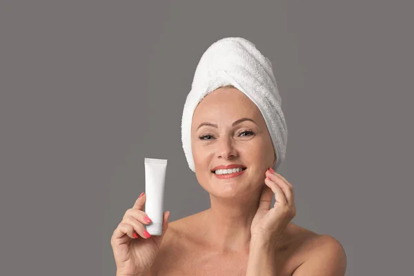 Portrait de belle femme mature avec tube de maintien parfait de la peau de crème sur fond gris — Photo