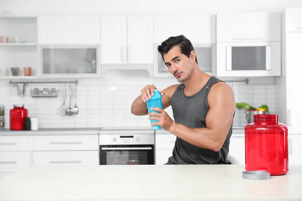 Homem atlético jovem com pó de batido de proteína na cozinha, espaço para texto — Fotografia de Stock