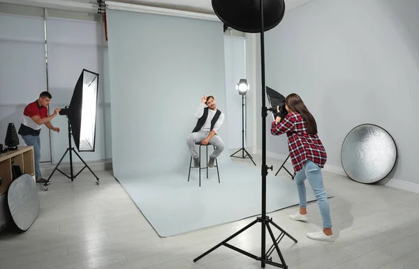 Fotógrafo profesional con asistente tomando fotos de un joven en un estudio moderno — Foto de Stock