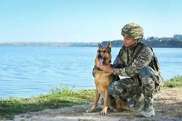 Muž v vojenské uniformě s německým ovčákem u řeky, prostor pro text — Stock fotografie