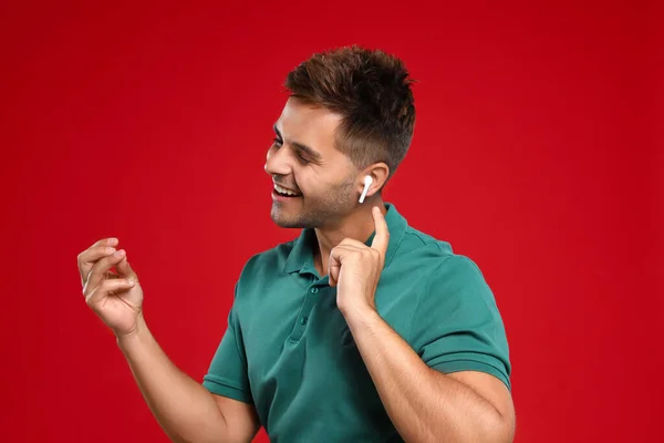 Jovem feliz ouvindo música através de fones de ouvido sem fio no fundo vermelho — Fotografia de Stock