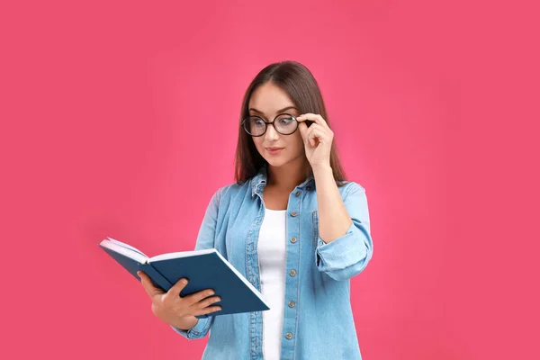Gyönyörű fiatal nő szemüveggel és könyv a bíbor háttér — Stock Fotó