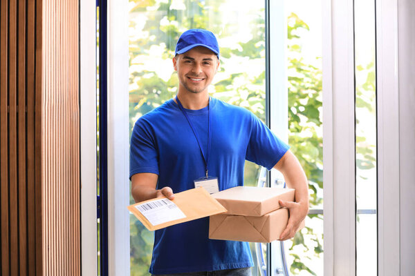 Young courier holding parcels on doorstep. Delivery service