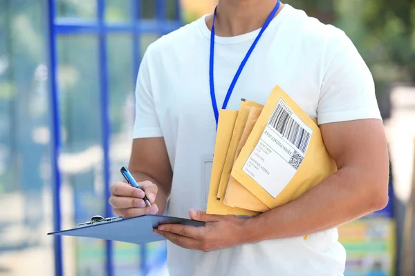 Correios jovens com envelopes acolchoados e prancheta ao ar livre, close-up. Serviço de entrega — Fotografia de Stock