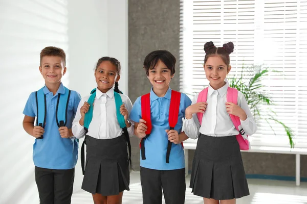 Crianças felizes em uniforme escolar com mochilas dentro de casa — Fotografia de Stock