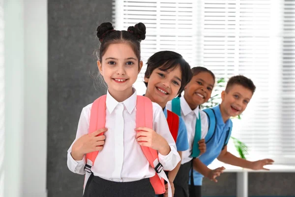 Gelukkige kinderen in school uniform met rugzakken binnenshuis — Stockfoto