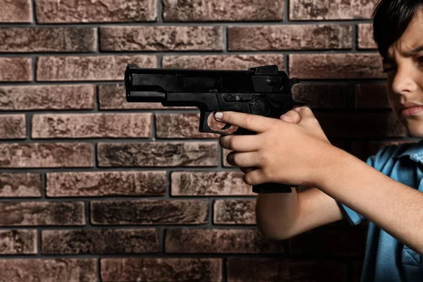 Criança brincando com arma contra parede de tijolo. Jogo perigoso — Fotografia de Stock
