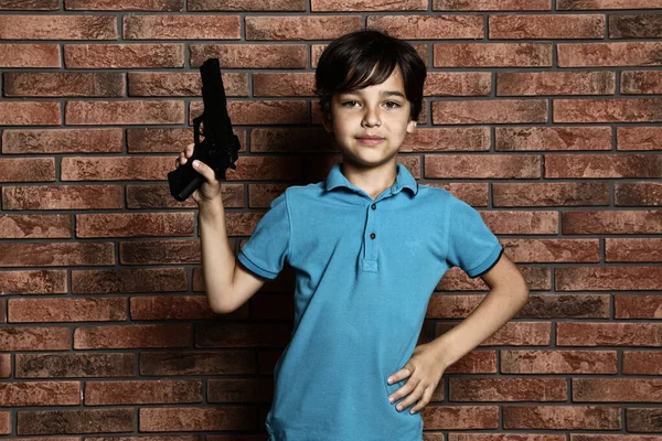 Criança brincando com arma contra parede de tijolo. Jogo perigoso — Fotografia de Stock