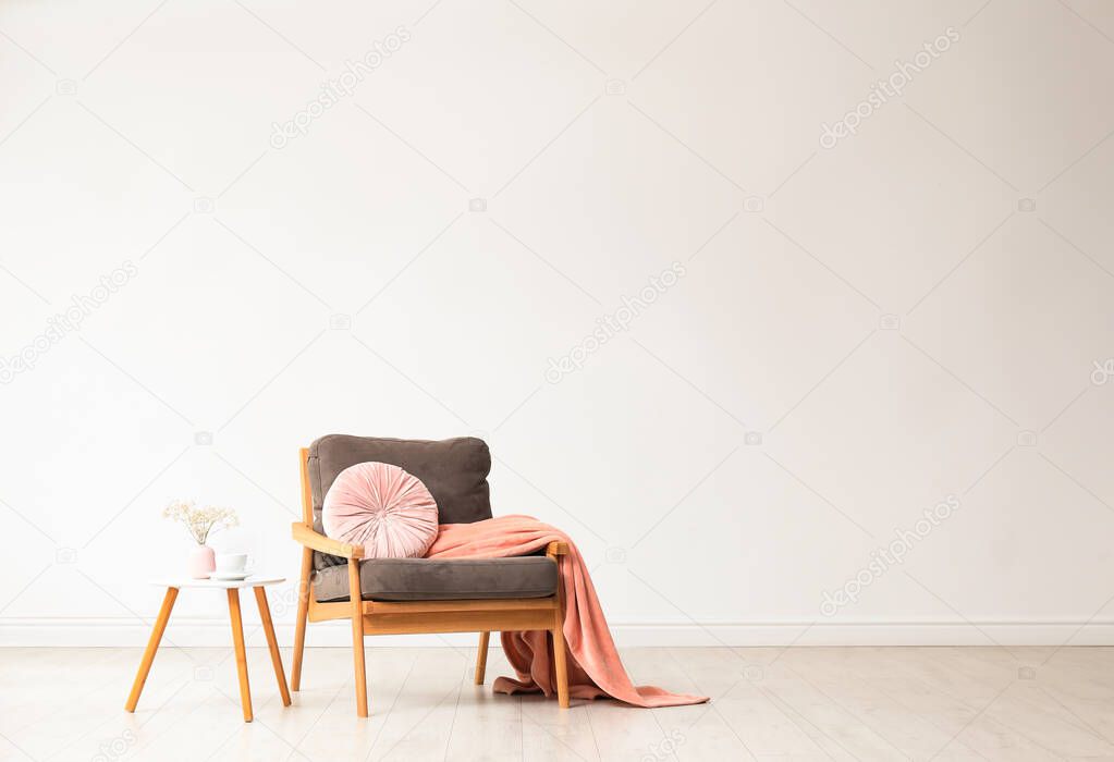 Stylish living room interior with comfortable armchair and wooden table near white wall. Space for text